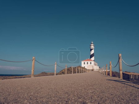 Téléchargez les photos : Passerelle vide avec clôture en bois menant au phare blanc sous un ciel bleu sans nuages par temps ensoleillé - en image libre de droit