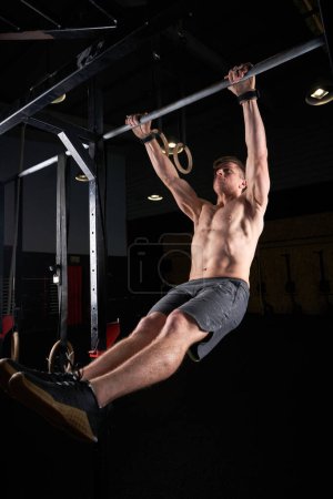 Téléchargez les photos : Corps complet de l'athlète masculin fort avec torse nu faisant pull-ups sur la barre pendant l'entraînement dans la salle de gym - en image libre de droit