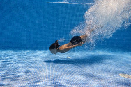 Téléchargez les photos : Vue latérale de l'enfant préadolescent entouré de bulles d'air s'amuser tout en plongeant dans la piscine bleue le week-end jour d'été - en image libre de droit