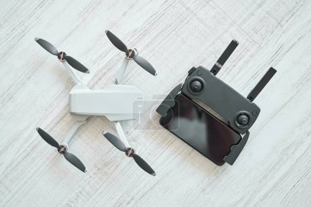 Téléchargez les photos : Vue de dessus du drone moderne sans pilote et du panneau de commande à distance placés sur un plancher stratifié léger - en image libre de droit