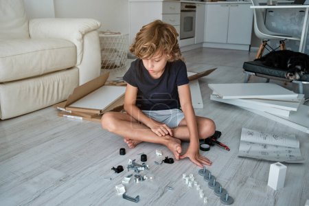 Photo for Full body of concentrated boy in casual clothes sitting on floor with legs crossed and sorting fasteners in living room at home - Royalty Free Image