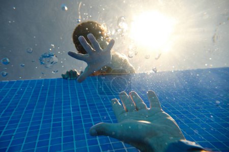 Foto de Bajo ángulo de hijo apoyado en el borde de la piscina de azulejos en el complejo y llegar a las manos con el padre de la cosecha en fin de semana día de verano - Imagen libre de derechos