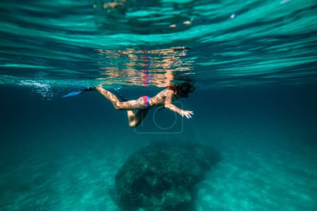Foto de Vista lateral de cuerpo completo adolescente anónimo flotando en agua de mar azul profundo en aletas y máscara de snorkel - Imagen libre de derechos