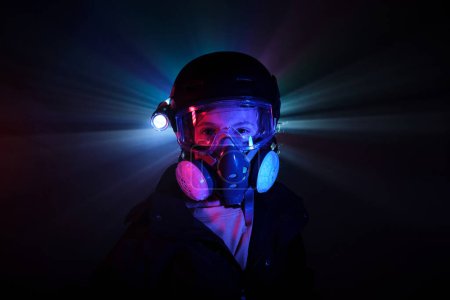 Photo for Boy in protective respirator with shining flashlight looking at camera while standing in dark mint with neon lights during illegal heist - Royalty Free Image