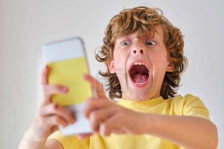 Foto de Niño asustado con la boca abierta gritando mientras toma autorretrato en el teléfono celular durante el día - Imagen libre de derechos