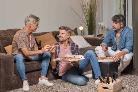 Téléchargez les photos : Heureux hommes mûrs en vêtements décontractés manger de délicieuses pizzas tout en s'amusant dans le salon à la maison - en image libre de droit