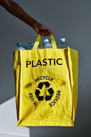 Téléchargez les photos : Crop anonyme volontaire femelle tenant sac jaune avec des bouteilles en plastique triées pour le recyclage et le nettoyage de l'environnement de la poubelle - en image libre de droit