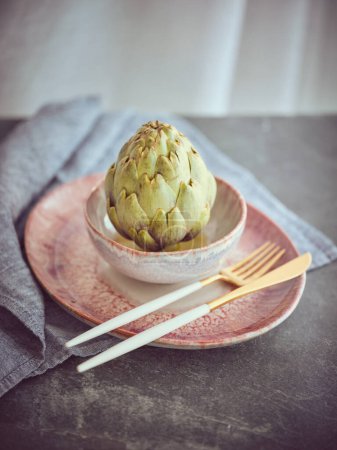 Foto de Sabroso brote de alcachofa verde saludable con hojas servidas en el plato con cubiertos en la mesa con toalla gris en la cocina ligera - Imagen libre de derechos