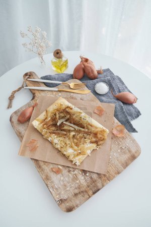 Téléchargez les photos : D'en haut de savoureuse tarte feuilletée aux oignons cuits au four servie sur planche à découper avec parchemin dans la cuisine légère à la maison - en image libre de droit