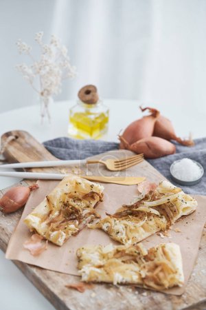 Téléchargez les photos : Tarte à l'oignon fraîchement cuite servie sur une planche à découper en bois dans une cuisine légère avec des huiles et des fleurs séchées - en image libre de droit