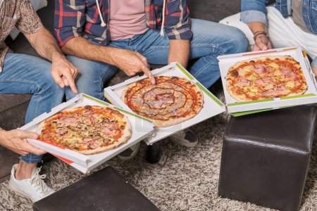 Photo for From above of crop anonymous male friends in casual clothes sitting in living room and pointing at different types of pizza - Royalty Free Image