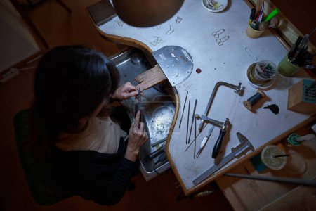 Foto de Vista superior de orfebre femenino irreconocible usando archivo de aguja mientras diseña joyas en la mesa durante el trabajo en el estudio tradicional - Imagen libre de derechos