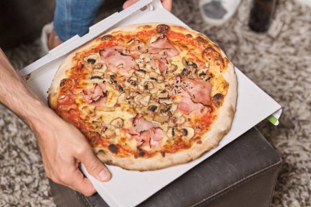 Téléchargez les photos : De dessus de la boîte de carton d'exploitation masculine anonyme de récolte avec pizza pour aller avec des champignons et du jambon à la maison - en image libre de droit