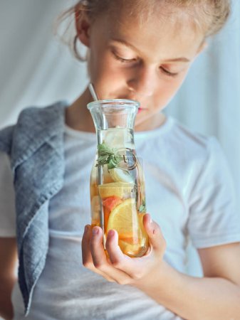 Téléchargez les photos : Culture d'enfant avec bouteille remplie de limonade savoureuse faite de pamplemousse citron orange et d'épices - en image libre de droit