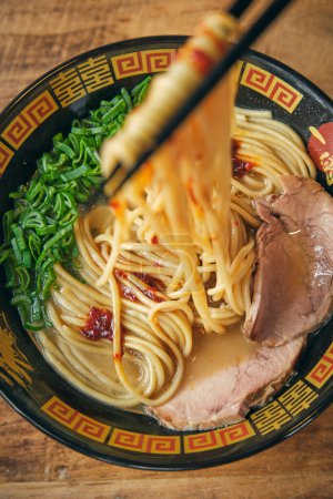 Photo for Top view of tasty Japanese soup with chopped green onions and pork slices in broth under noodles on food sticks - Royalty Free Image