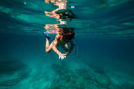 Foto de Cuerpo completo de nadador adolescente anónimo buceando en agua de mar turquesa profunda en máscara de snorkel y aletas - Imagen libre de derechos