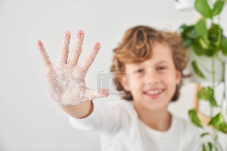 Téléchargez les photos : Concentration sélective de la paume du garçon gai nettoyer les mains avec du savon tout en faisant la routine d'hygiène quotidienne le matin - en image libre de droit