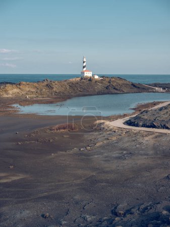 Photo for Picturesque scenery of white lighthouse located on rocky coastline surrounded by blue ocean under cloudless blue sky in daytime - Royalty Free Image