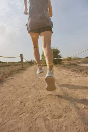 Photo for Crop anonymous female athlete in shorts and sneakers running on sandy path near field on sunny summer day - Royalty Free Image