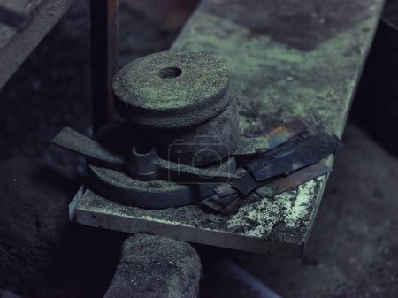 Foto de Alto ángulo de la rueda de molienda de metal y parte del pico colocado en yunque polvoriento en taller de forja gruesa - Imagen libre de derechos