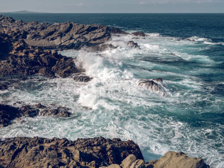 Foto de Impresionante paisaje de poderoso mar azul espumoso lavado costa rocosa áspera en el día - Imagen libre de derechos