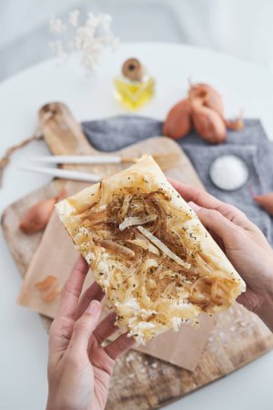 Photo for From above hands of crop anonymous person holding slice of freshly baked puff pastry onion tart above table with cutting board - Royalty Free Image