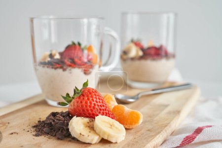 Téléchargez les photos : Tranches de banane mandarine et fraise servies sur planche à découper en bois avec dessert appétissant servi dans des verres au chocolat et au yaourt - en image libre de droit