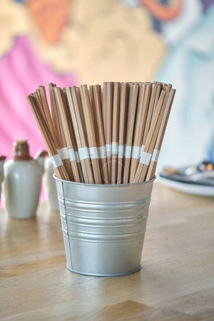 Photo for Set of wooden chopsticks for sushi in metal bucket placed on wooden table in light cafe with colorful painter wall - Royalty Free Image