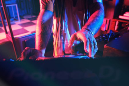 Foto de Crop DJ masculino anónimo en ropa casual que reproduce música en el reproductor de CDJ moderno mientras trabaja en un club nocturno con poca iluminación - Imagen libre de derechos