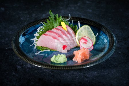 Foto de Delicioso sashimi de pescado de cola amarilla servido en el plato con rodaja de lima y wasabi con jengibre en la mesa en el restaurante - Imagen libre de derechos