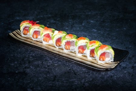 Photo for From above of appetizing tobiko roe with fresh green avocado slices on top of uramaki sushi rolls served on tray on marble counter - Royalty Free Image
