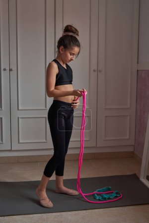 Foto de Vista lateral de cuerpo completo de niña preadolescente concentrada en ropa deportiva de pie en la estera y medir la longitud de la cuerda de salto antes del entrenamiento - Imagen libre de derechos