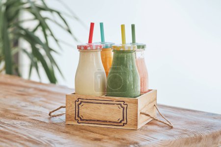 Téléchargez les photos : Ensemble de smoothies sains servis dans des bouteilles en verre avec des pailles colorées dans une boîte en bois sur la table - en image libre de droit