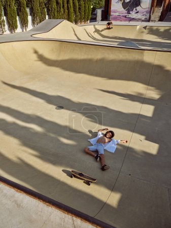 Foto de De arriba la longitud completa del chiquitín caído del longboard en skate park en el día soleado - Imagen libre de derechos
