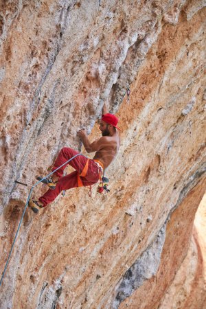 Foto de Vista lateral de cuerpo completo de un fuerte alpinista con torso desnudo escalando la ladera rocosa de la montaña con superficie rugosa desigual durante el entrenamiento en la naturaleza - Imagen libre de derechos
