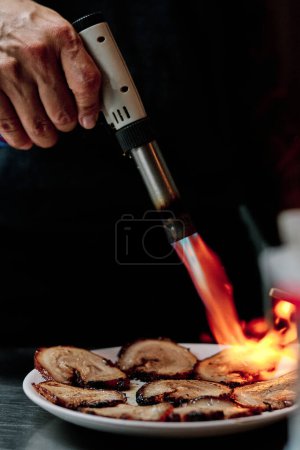 Téléchargez les photos : Photo stock de chef non reconnu utilisant la torche de cuisine dans le restaurant. - en image libre de droit