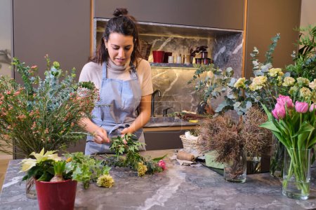 Téléchargez les photos : Jeune femme debout à la table de marbre avec diverses fleurs en fleurs et d'organiser des bouquets dans la boutique florale moderne - en image libre de droit