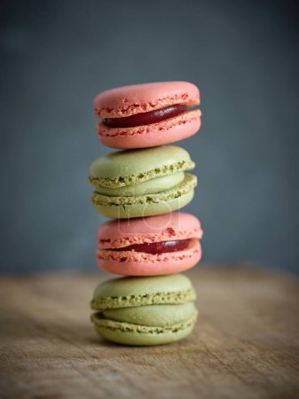 Photo for Delicious pistachio and strawberry flavored macaroons with sweet filling stacked on top of each other against gray background in room - Royalty Free Image