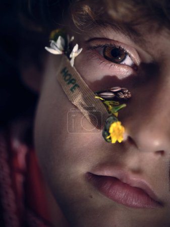 Téléchargez les photos : Recadrage visage d'enfant avec de minuscules fleurs clued par ruban adhésif regardant caméra sur fond flou - en image libre de droit