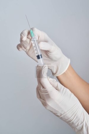 Foto de Manos de cultivo médico anónimo en guantes de látex que sostienen jeringa con vacuna contra fondo blanco en sala de luz durante la pandemia - Imagen libre de derechos
