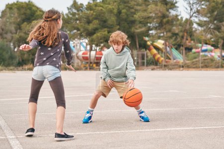 Téléchargez les photos : Adolescent garçon et fille jouer basket sur terrain de jeu tout en divertissant ensemble le week-end - en image libre de droit