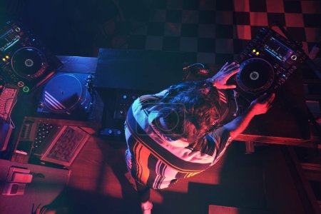 Foto de Desde arriba de un hombre irreconocible tocando música en la configuración moderna de DJ mientras trabaja en un club nocturno oscuro con equipo musical moderno - Imagen libre de derechos