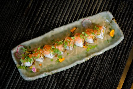 Téléchargez les photos : Vue du dessus des sushis uramaki au saumon et légumes frais à l'avocat servis sur un plateau en marbre avec des fleurs placées sur la table sur fond noir - en image libre de droit