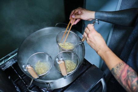 Téléchargez les photos : Photo de stock de nouilles de cuisine de chef non reconnu dans la cuisine du restaurant japonais. - en image libre de droit