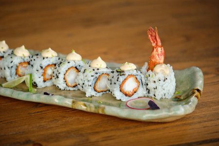 Foto de Deliciosos rollos de sushi con salmón y semillas de sésamo negro servidos en un plato colocado sobre una mesa de madera sobre un fondo borroso - Imagen libre de derechos