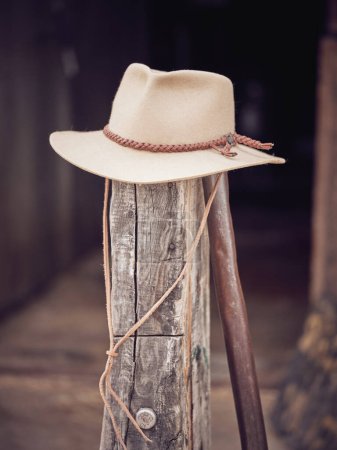 Foto de Sombrero vaquero beige con cordón colocado en la parte superior de la columna de madera en mal estado contra fondo borroso - Imagen libre de derechos