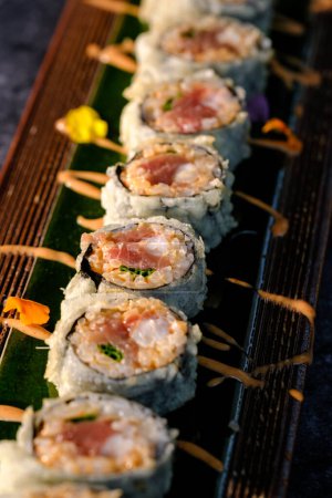 Foto de Desde arriba de surtidos rollos de sushi con pescado y arroz con crema de colores servidos en bandeja de madera sobre la mesa sobre fondo borroso - Imagen libre de derechos