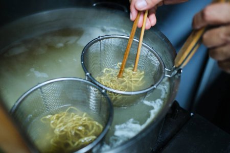 Photo for From above of crop anonymous person cooking noodles in water with chopsticks for tasty ramen - Royalty Free Image