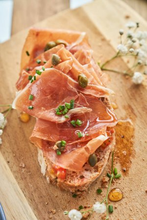 Photo for From above of appetizing toast with yummy prosciutto capers and olive oil served on wooden cutting board in restaurant - Royalty Free Image