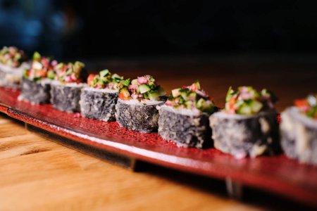 Foto de Composición de primer plano de deliciosos rollos servidos en placa roja de cerámica sobre la mesa en fondo oscuro - Imagen libre de derechos